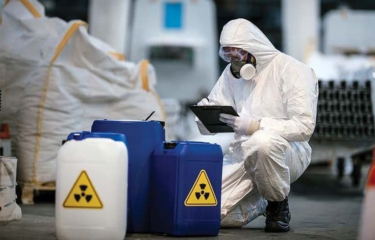 Technician in protective coveralls and respirator checking chemical containers